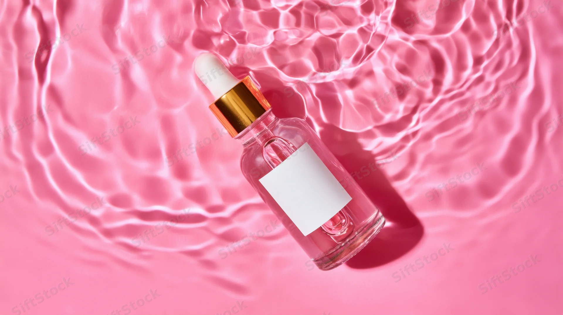 Clear glass dropper bottle with gold cap floating in rippling pink water