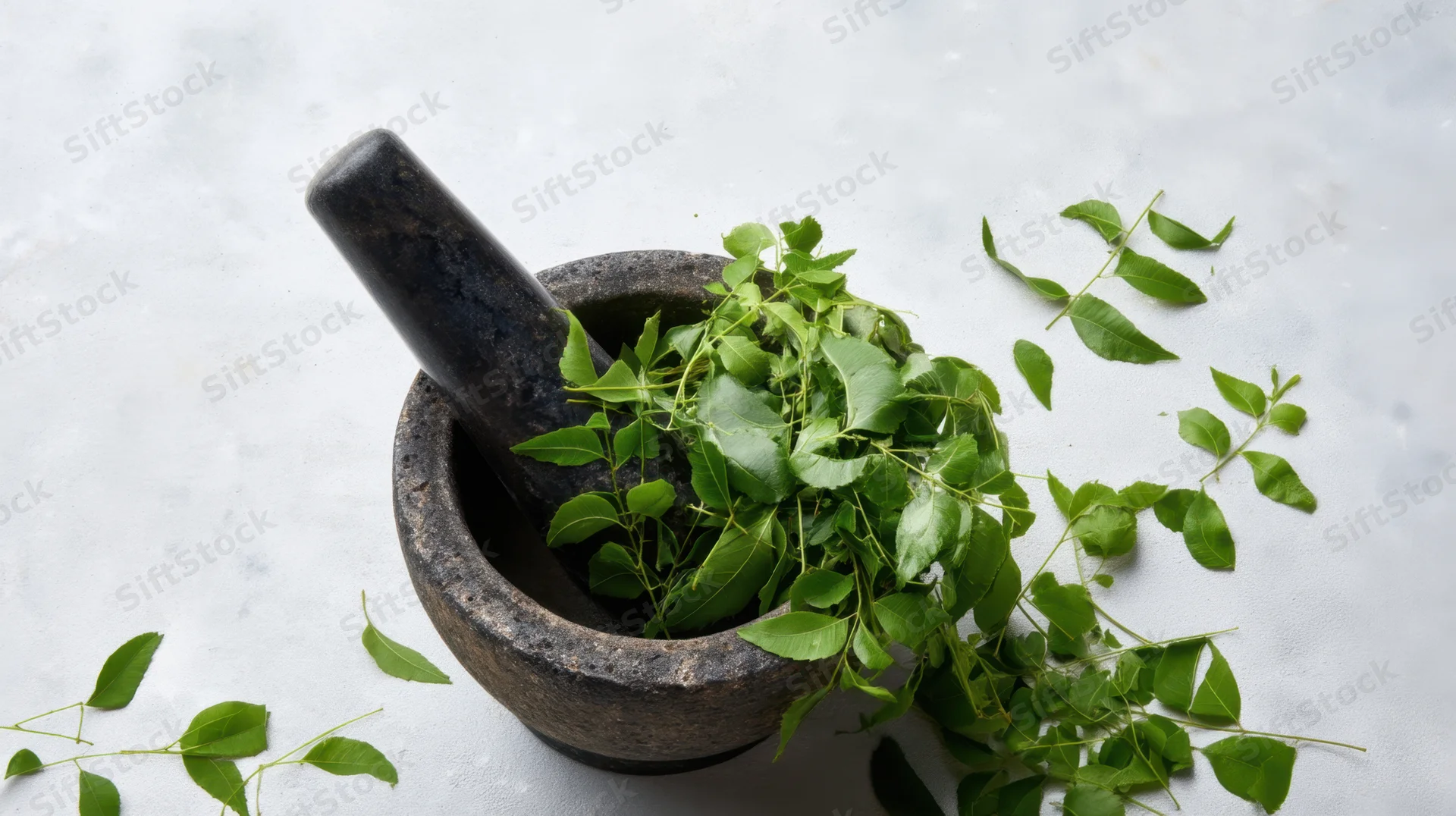Dark stone mortar and pestle filled with fresh green neem leaves on a light surface