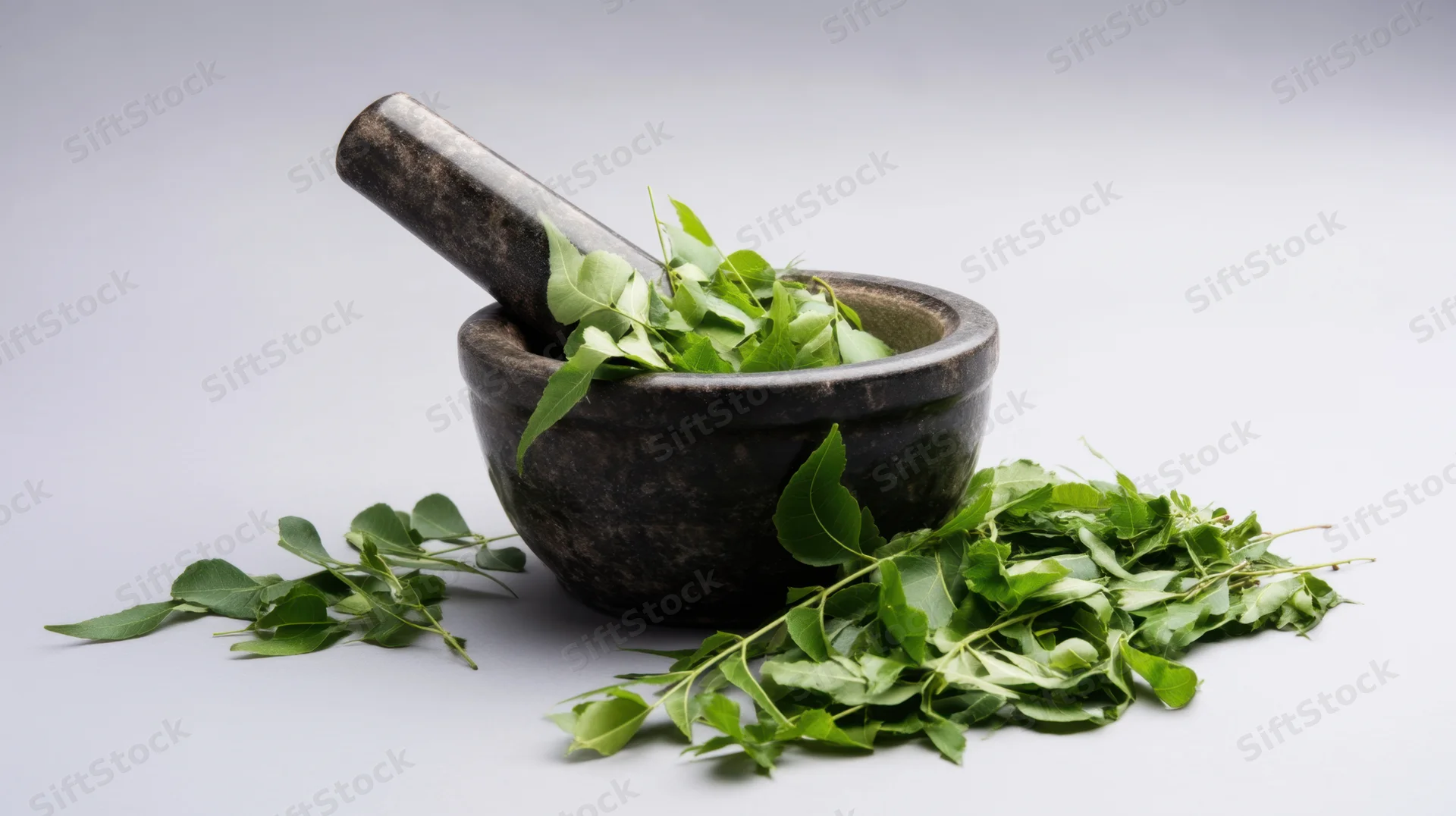 Dark stone mortar and pestle with fresh green neem leaves arranged on white surface