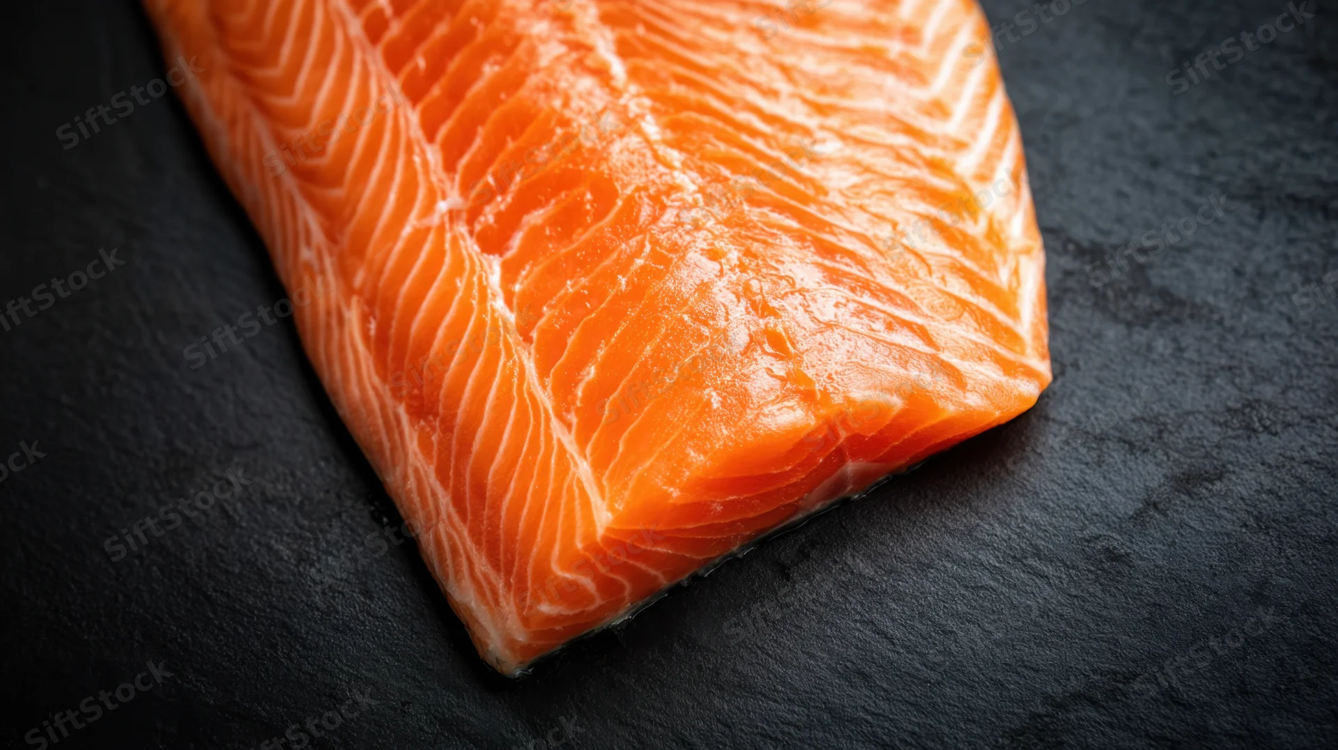 Fresh salmon fillet resting on dark slate surface