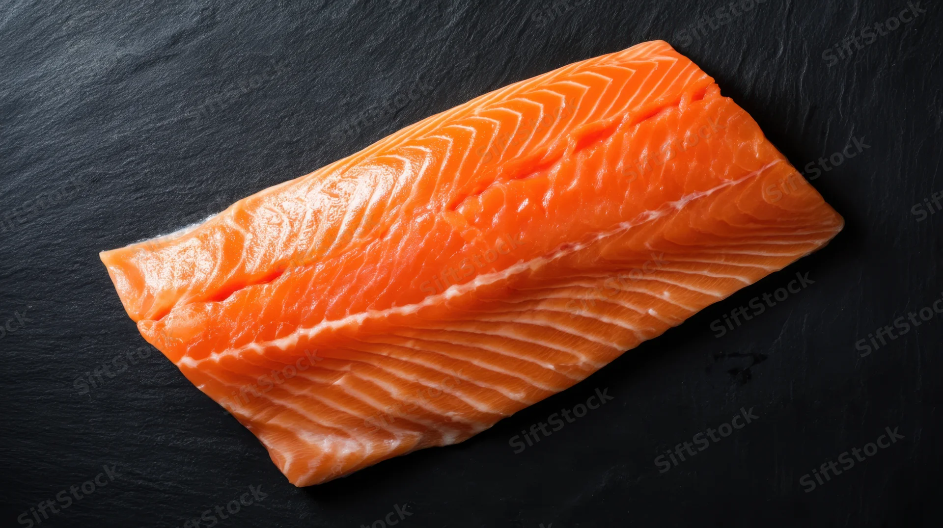 Fresh salmon fillet resting on dark slate surface