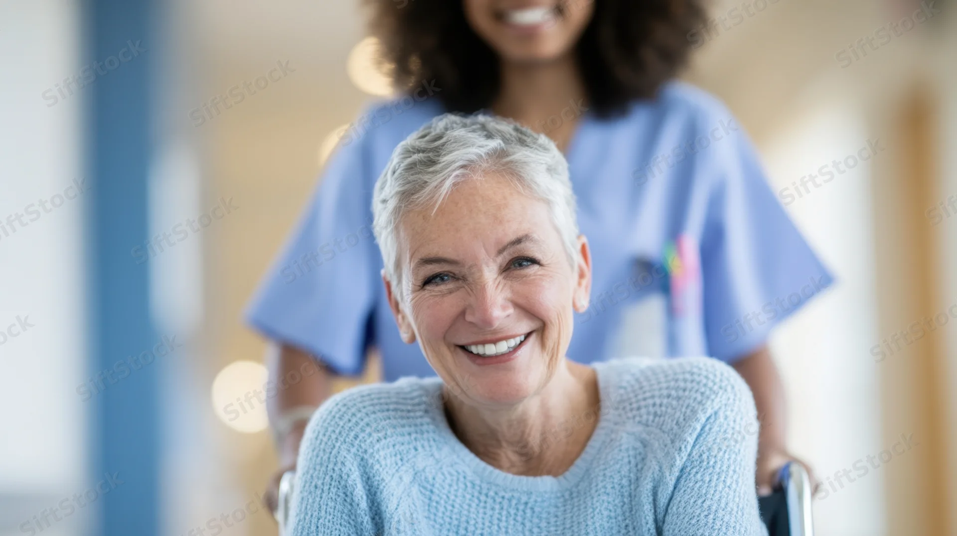 Senior woman smiling in wheelchair with nurse assisting in hospital corridor