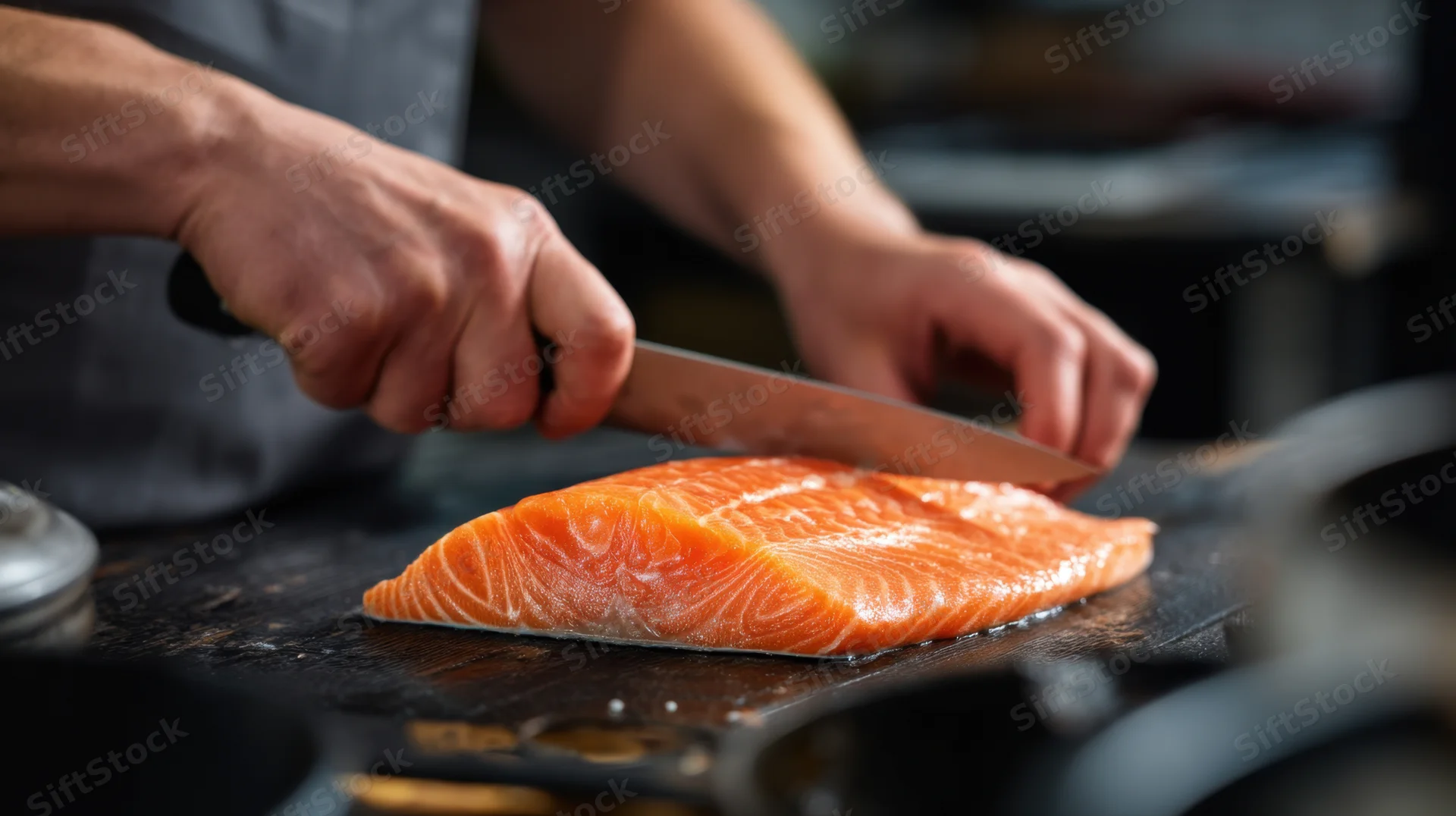 Chef filleting fresh salmon with a sharp knife on a dark cutting board in a professional kitchen