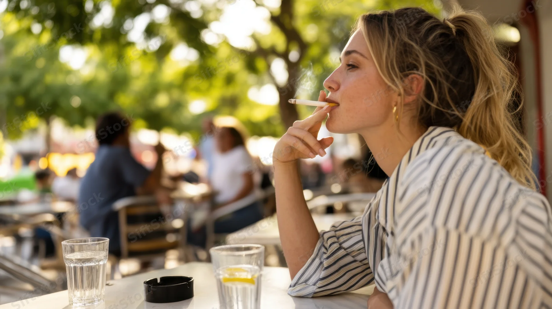 Young woman smoking a cigarette at an outdoor cafe table with glasses of water and lemon slices