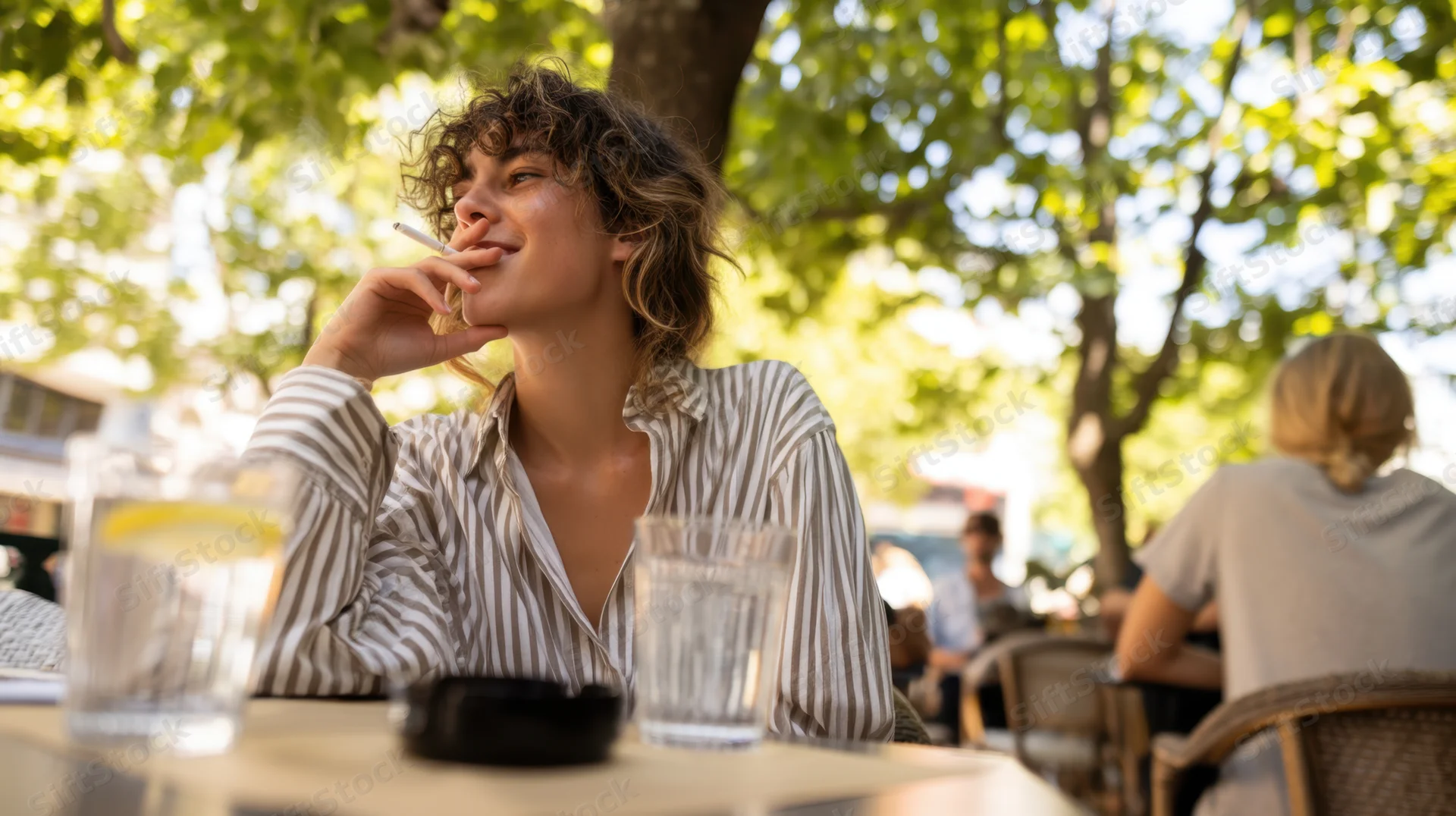 Young woman smoking a cigarette at an outdoor cafe table with glasses of water and lemon