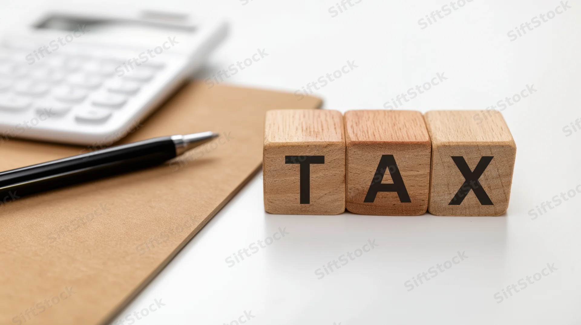 Wooden blocks spelling tax on a desk with calculator and pen nearby