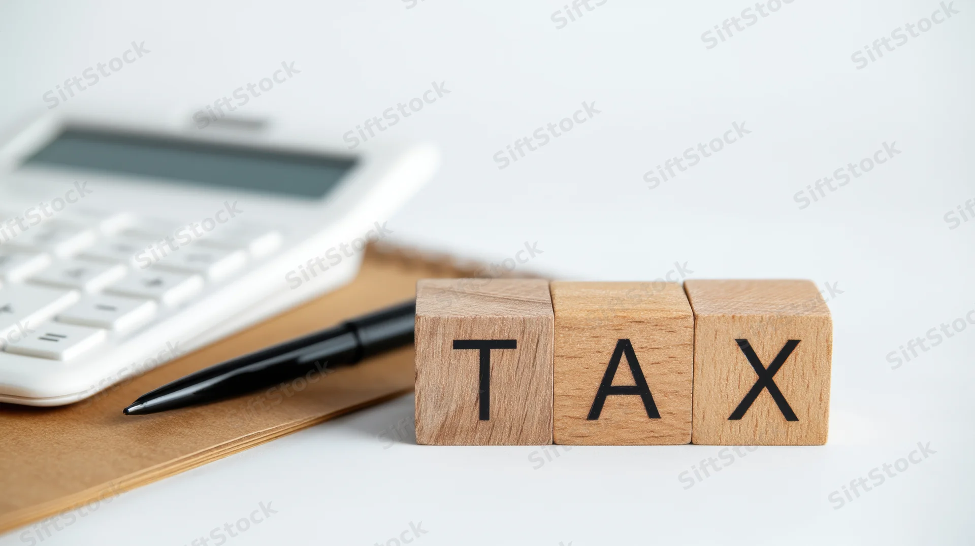 Wooden blocks spelling tax on a desk with calculator and pen nearby