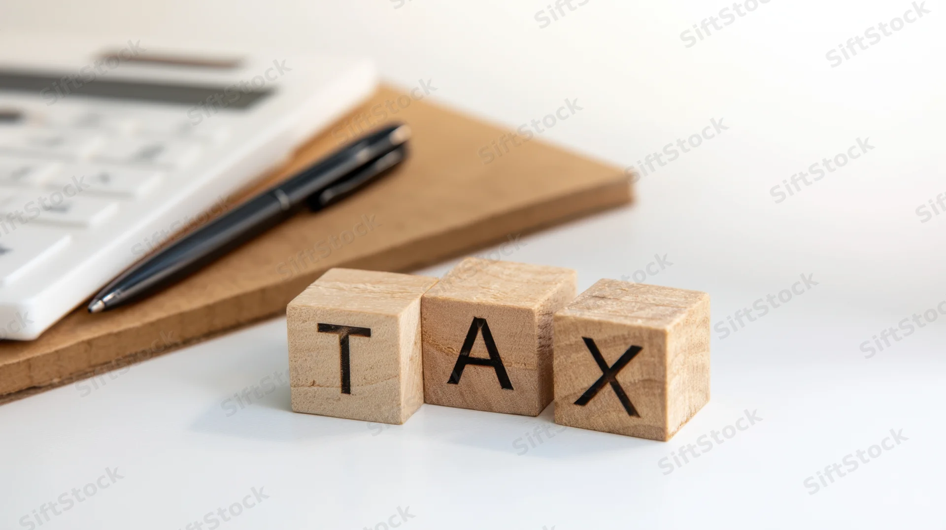 Wooden blocks spelling tax on a desk with calculator and pen nearby