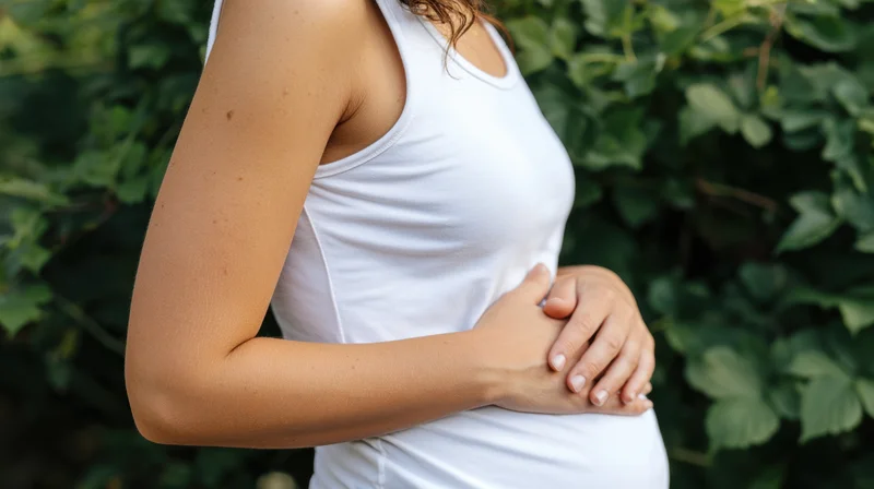 Pregnant woman with hands gently resting on her belly outdoors among green foliage