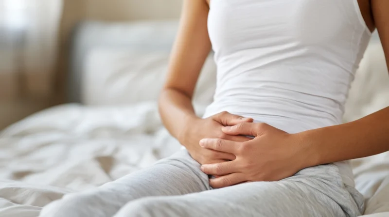 Woman sitting on bed with hands on abdomen showing discomfort