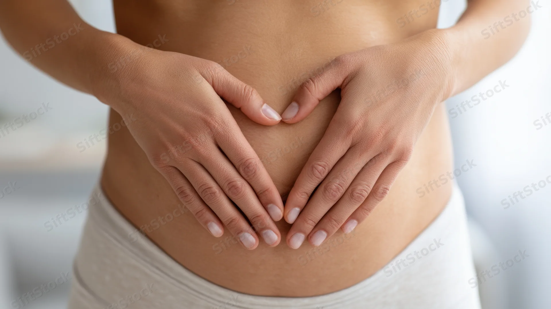 Woman’s midsection with hands forming heart shape over belly