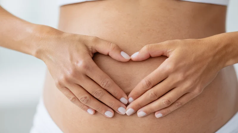 Woman’s midsection with hands forming heart shape over belly