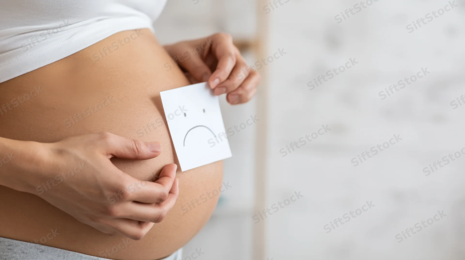 Pregnant woman holding paper with sad face on her belly