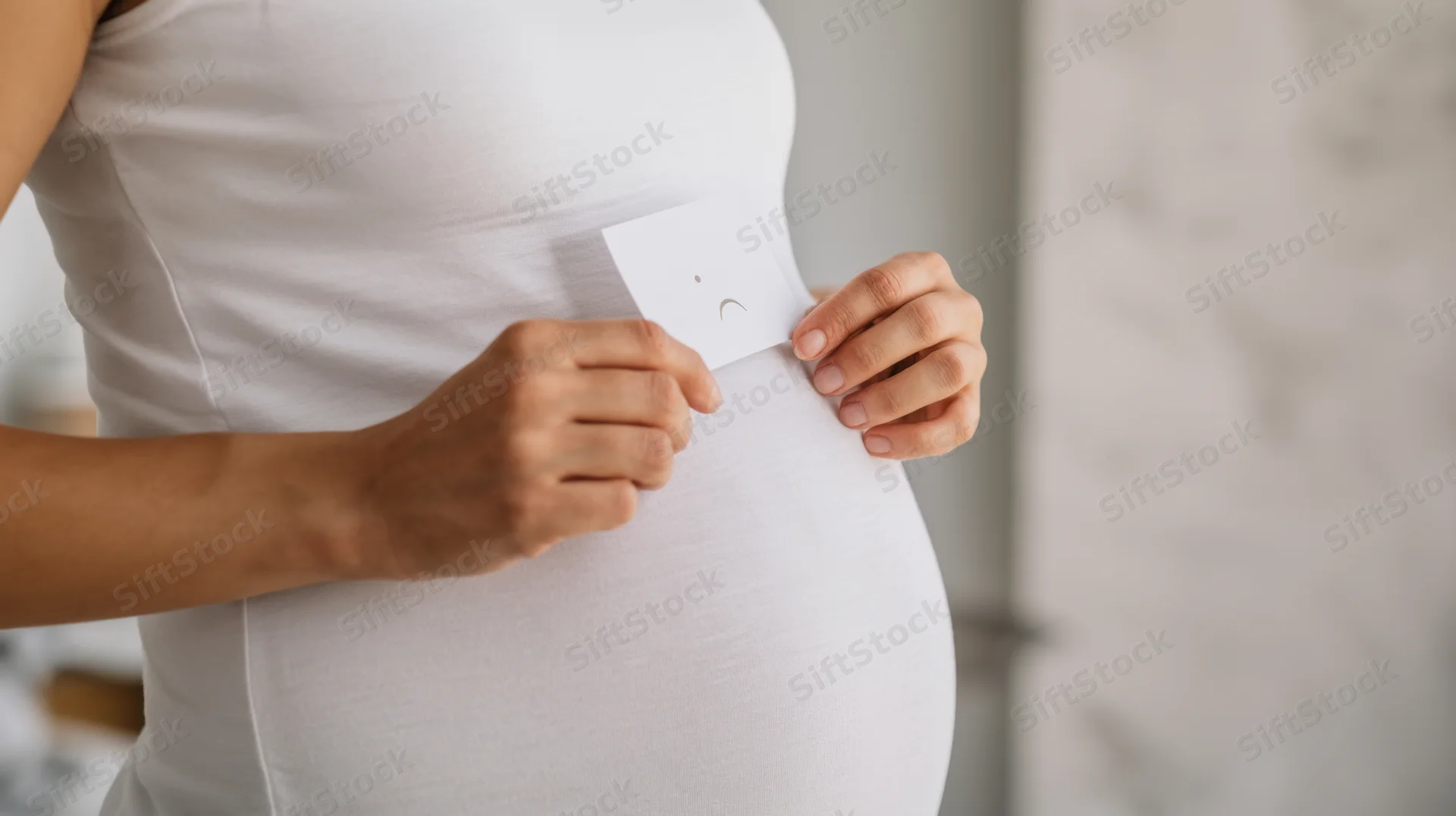 Pregnant woman holding sad face symbol on her belly indoors