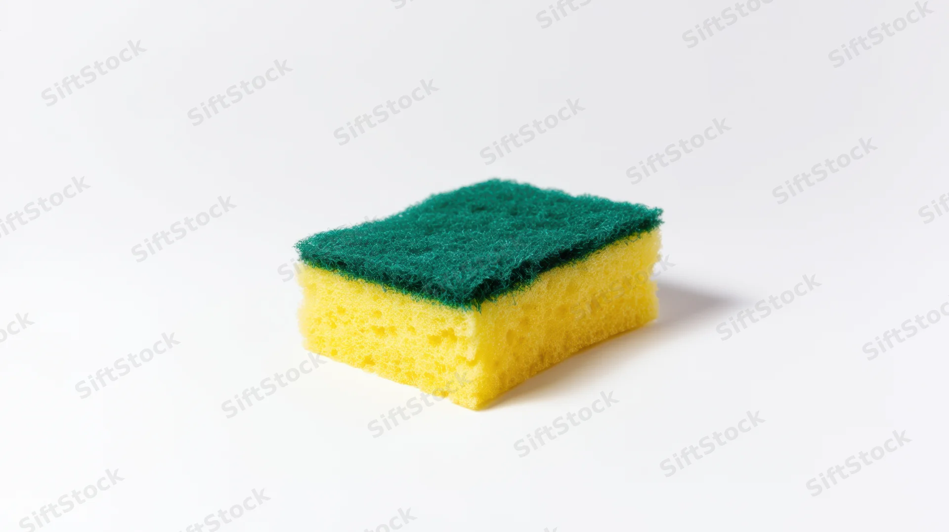 Yellow and green kitchen sponge with textured scrubbing side on white background