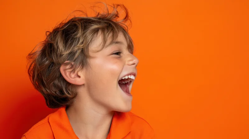 Young boy screaming loudly in profile against orange background wearing orange polo shirt