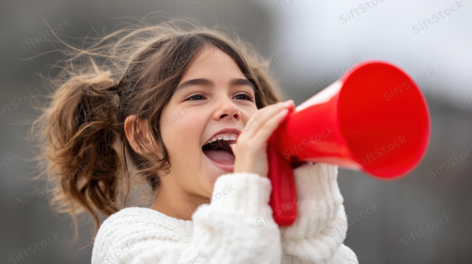 Young girl shouting into a red megaphone outdoors