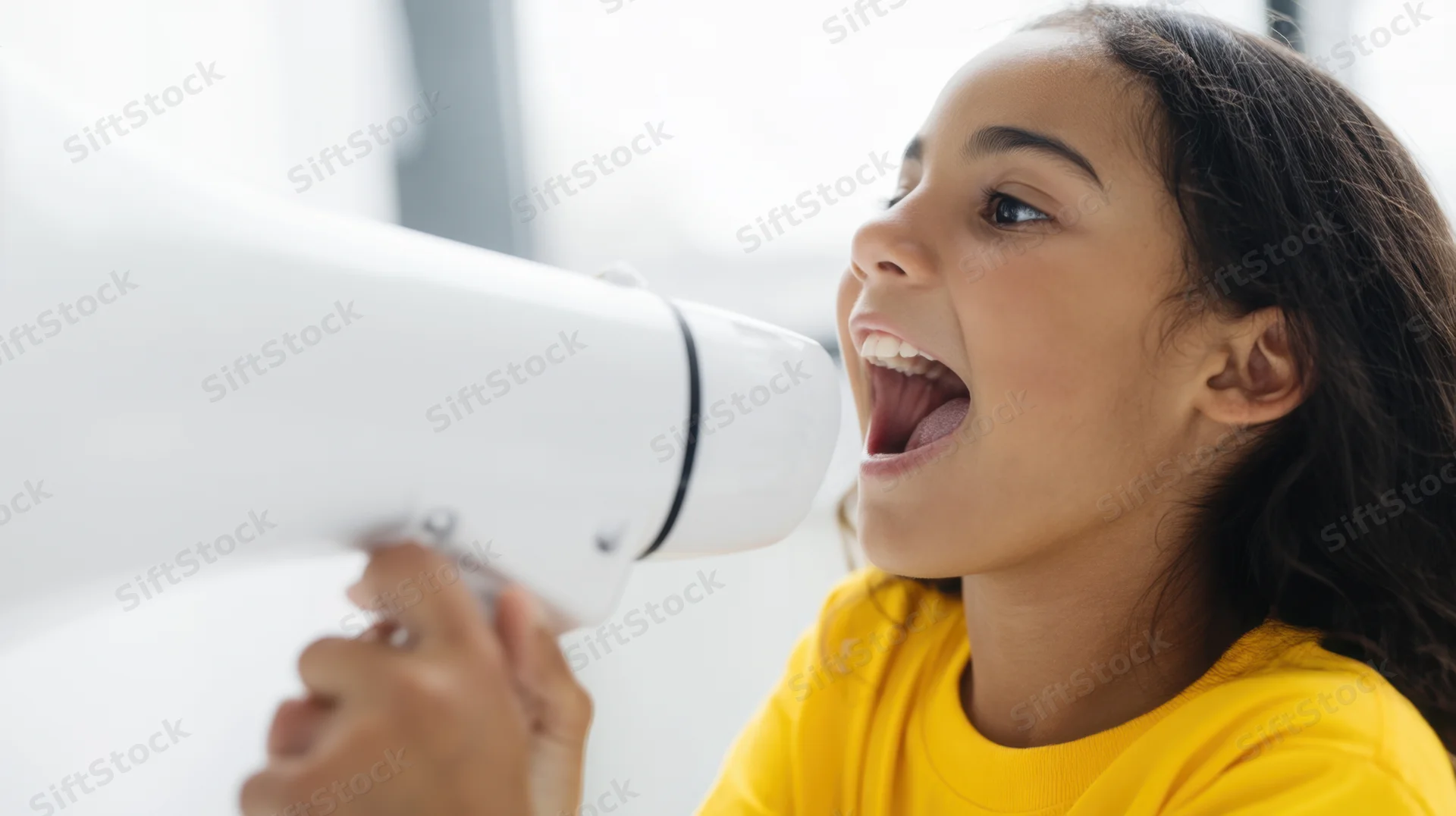 Young girl shouting into a white megaphone indoors, wearing a yellow tshirt