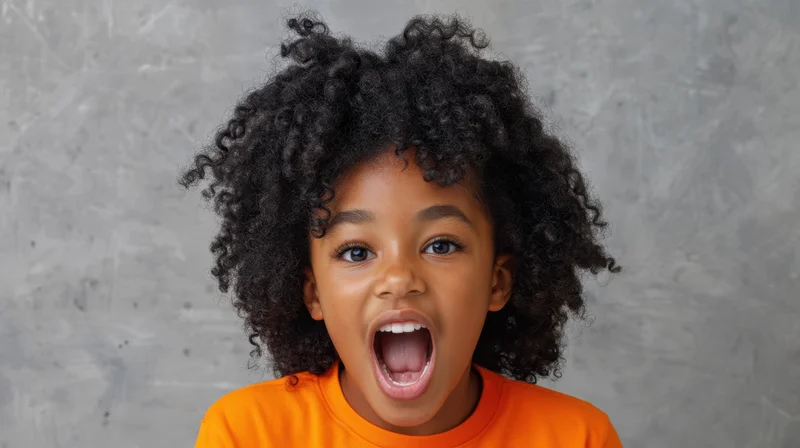 Young black girl with curly hair expressing surprise in studio portrait wearing orange shirt