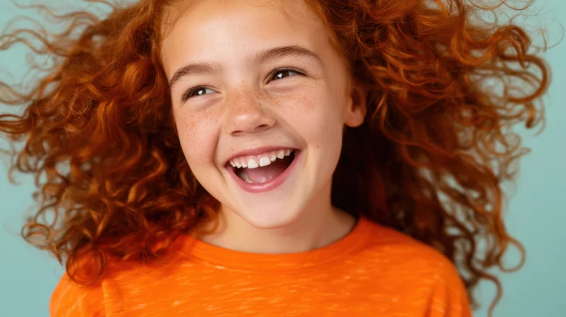 Young girl with vibrant curly red hair laughing joyfully in studio portrait