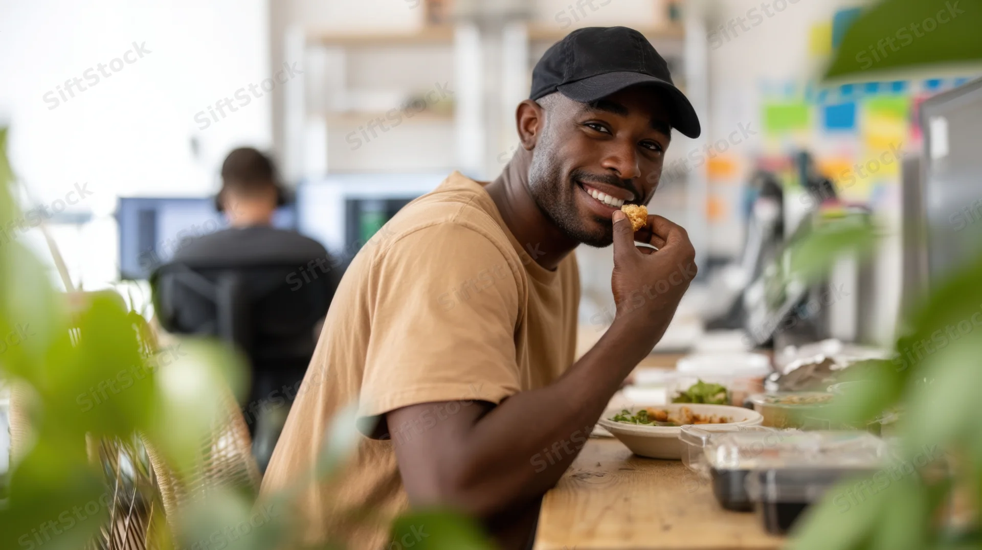 Young black man smiling while eating a meal from a bowl at his office desk