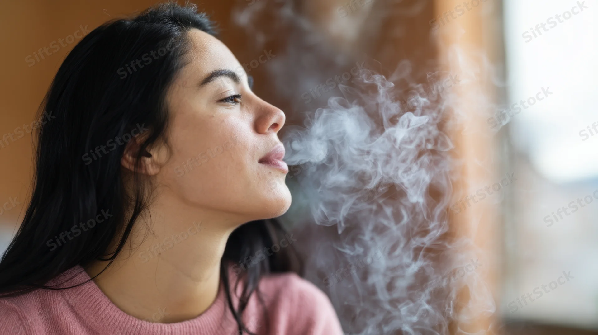 Young woman exhaling smoke in profile view indoors with soft natural light and blurred background