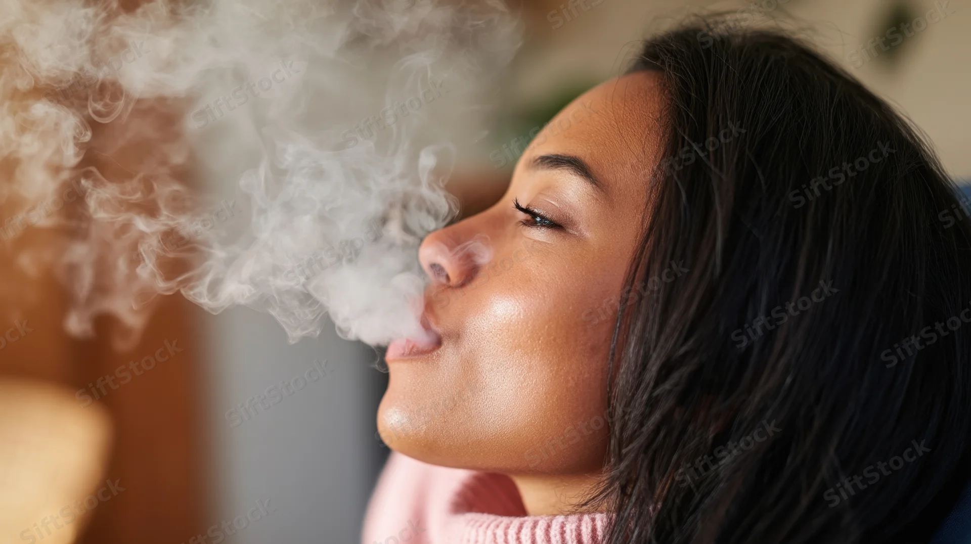 Young woman exhaling vapor while wearing a pink sweater indoors