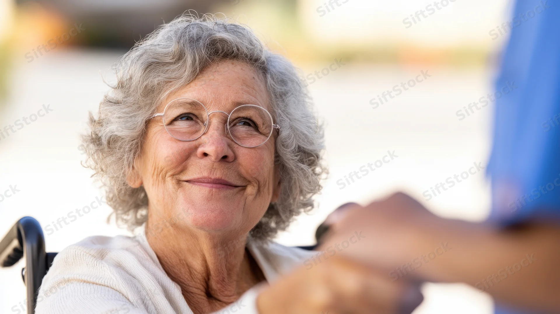 Elderly woman smiling while seated in wheelchair during outdoor interaction with caregiver