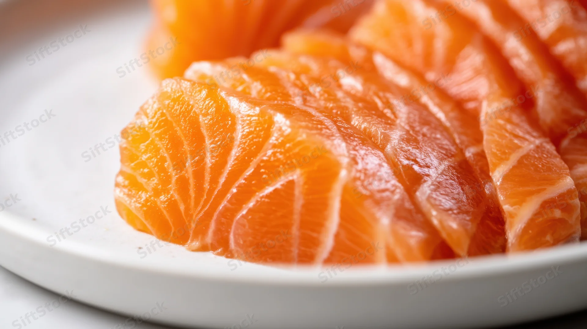 Freshly sliced salmon sashimi arranged on a white plate in closeup view