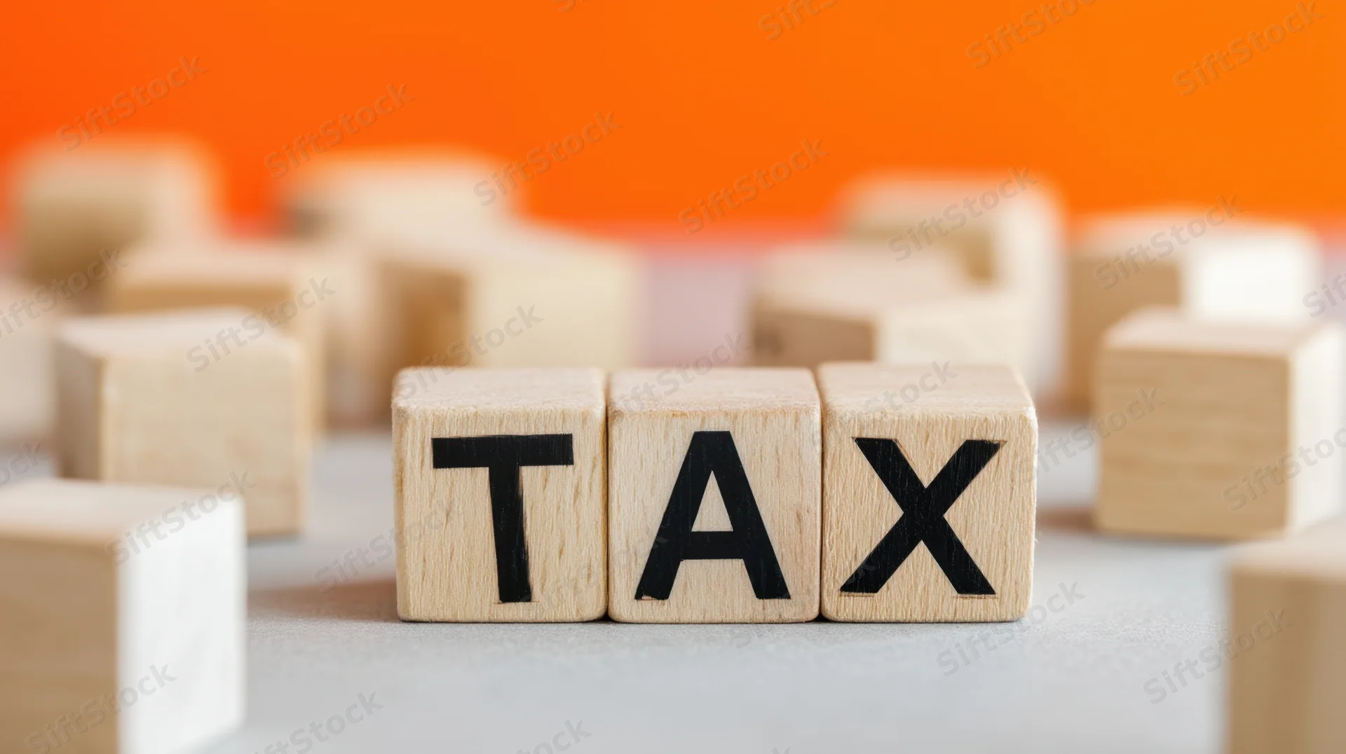 Wooden blocks arranged to spell tax on a light surface with orange background and scattered cubes around