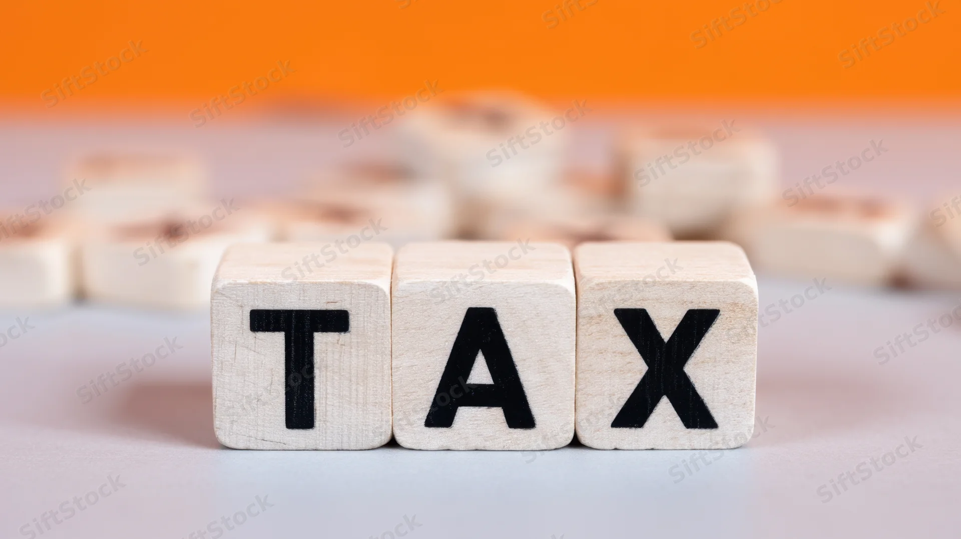 Wooden blocks arranged to spell tax on a gray surface with orange background