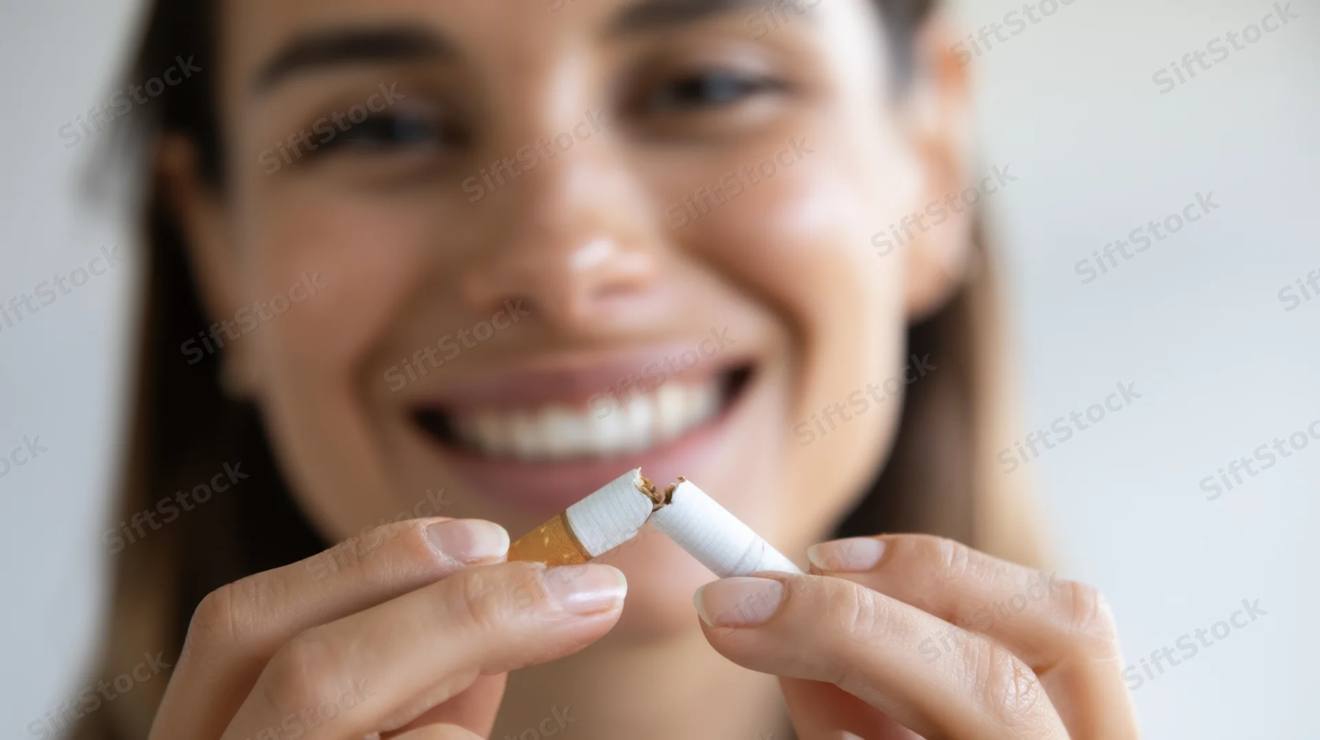 Woman smiling while holding broken cigarette in hands