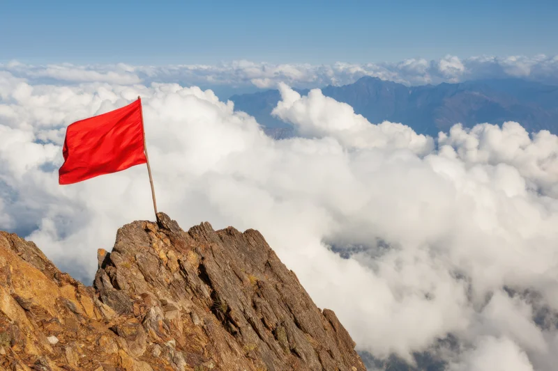 Red flag planted on rugged mountain peak above clouds