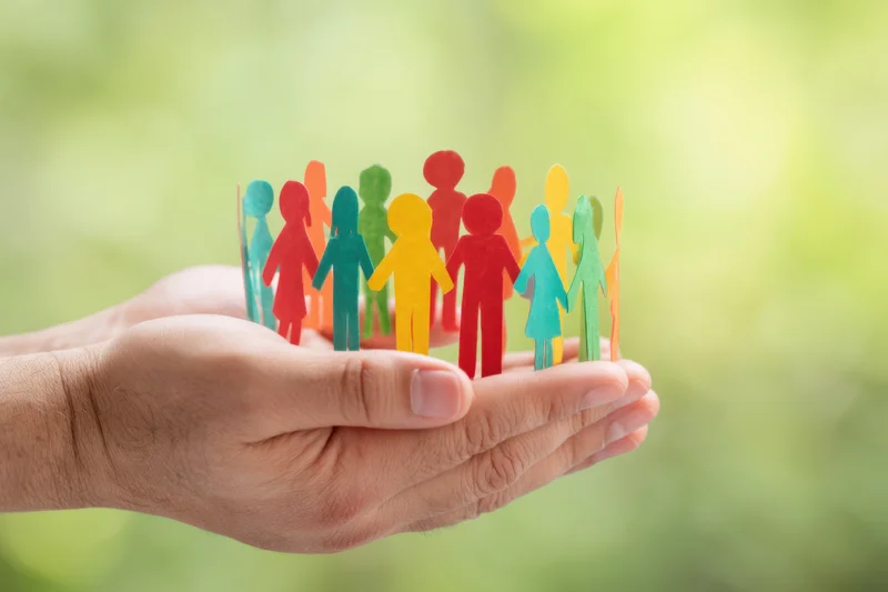 Hands holding colorful paper cutout people in a circle against a blurred green background
