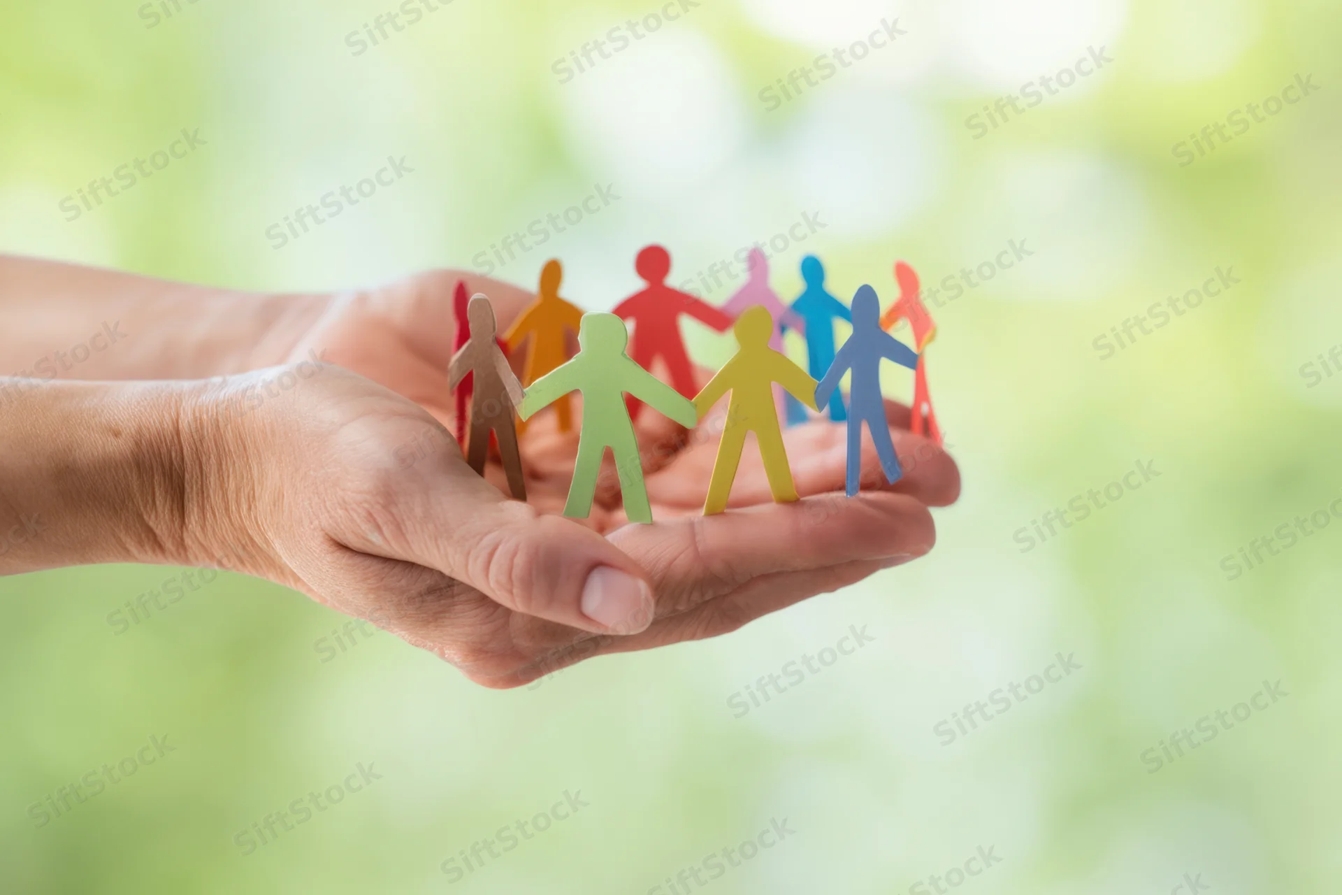 Hands holding colorful paper figures in a circle against a blurred green background