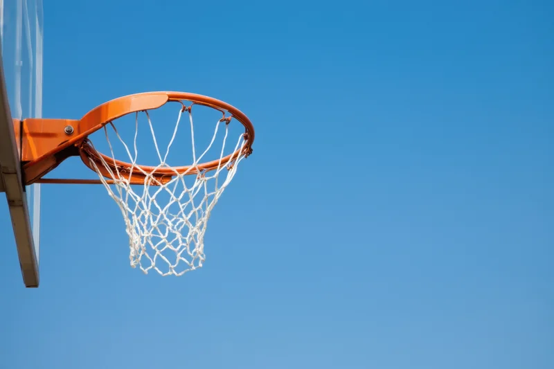 Basketball hoop with white net and orange rim against clear blue sky