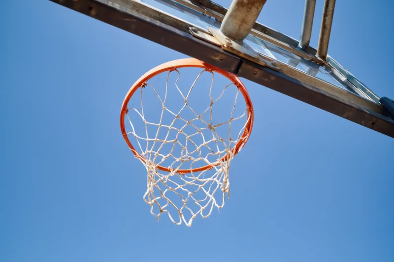 Basketball hoop with white net and orange rim against clear blue sky