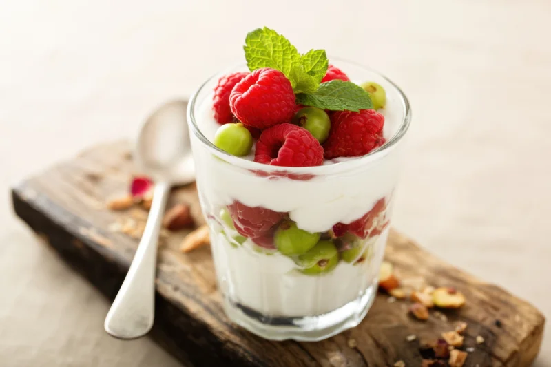 Layered yogurt parfait with raspberries and mint in a glass cup on a wooden board