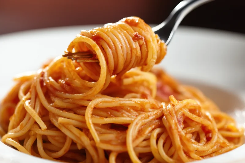 Spaghetti twirled on a fork above a plate of pasta with tomato sauce