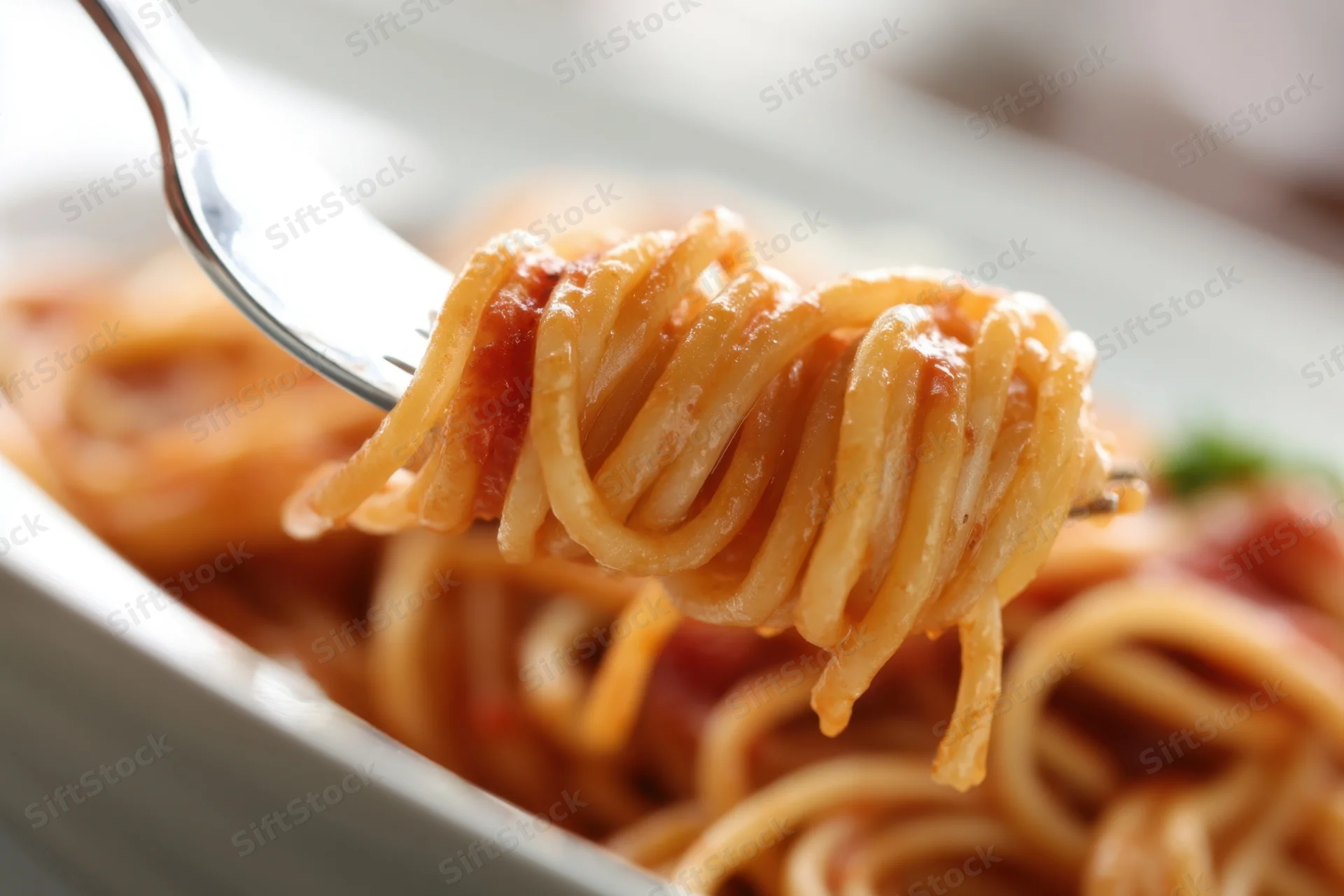 Spaghetti twirled on a fork above a bowl of tomato sauce pasta