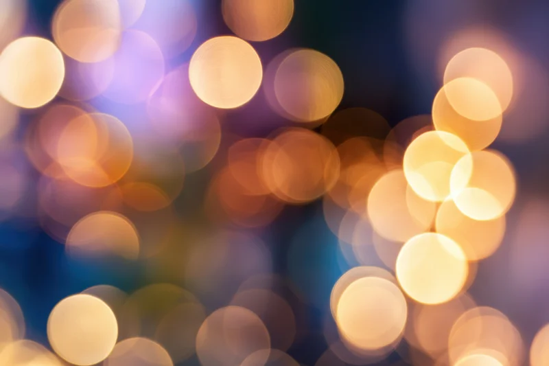 Blurred warm glowing orbs arranged in soft circular bokeh against a dark background with hints of blue and purple hues