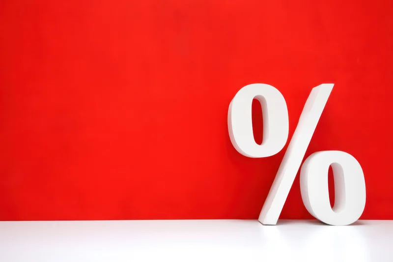 Bold white percentage symbol leaning against red wall on white surface