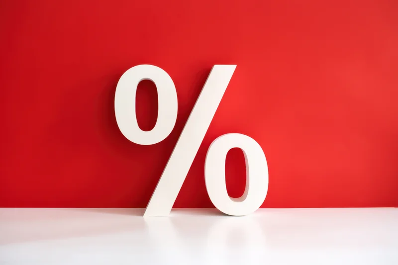 Bold white percentage symbol leaning against red wall on white surface