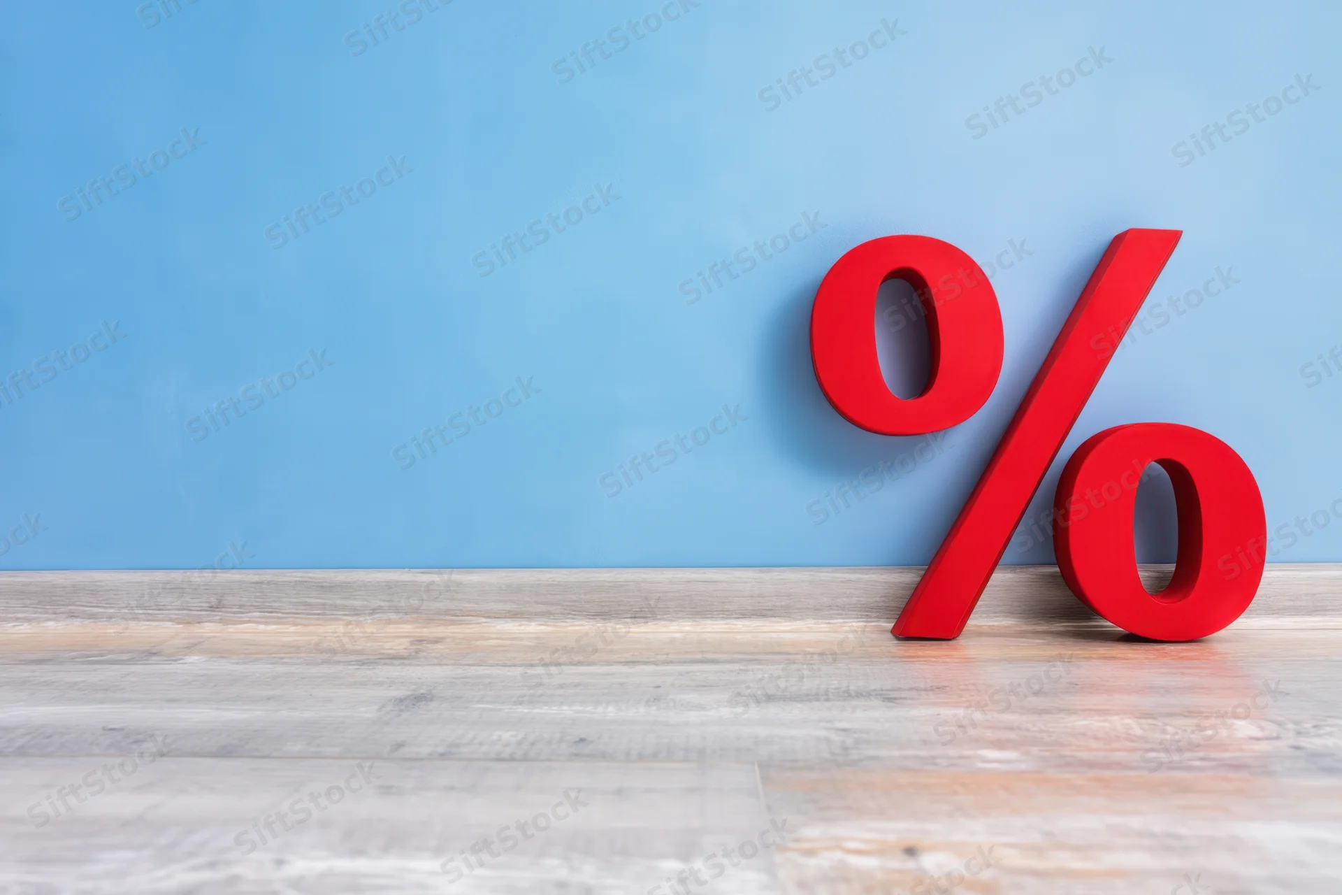 Red percentage symbol leaning against blue wall on wooden floor