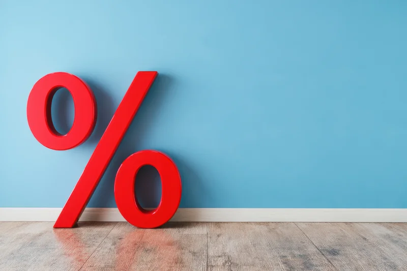 Red percentage symbol leaning against blue wall on wooden floor