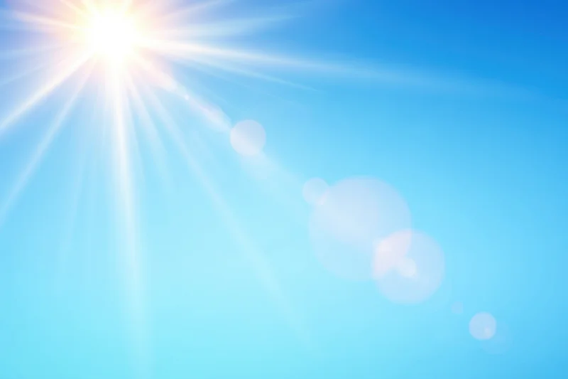 Bright sun shining in a clear blue gradient sky with lens flare and bokeh effects