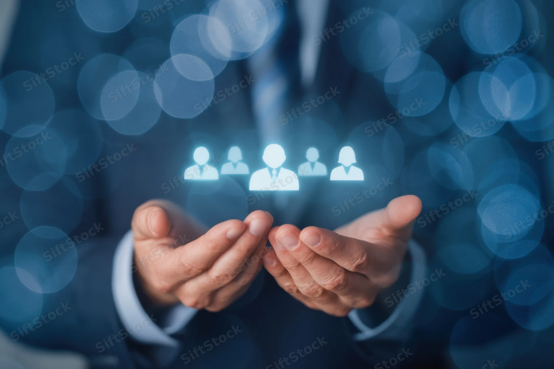 Business professional in suit holding glowing hologram of people icons with bokeh background