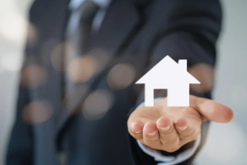 Business professional in suit holding hand out with house symbol floating above palm