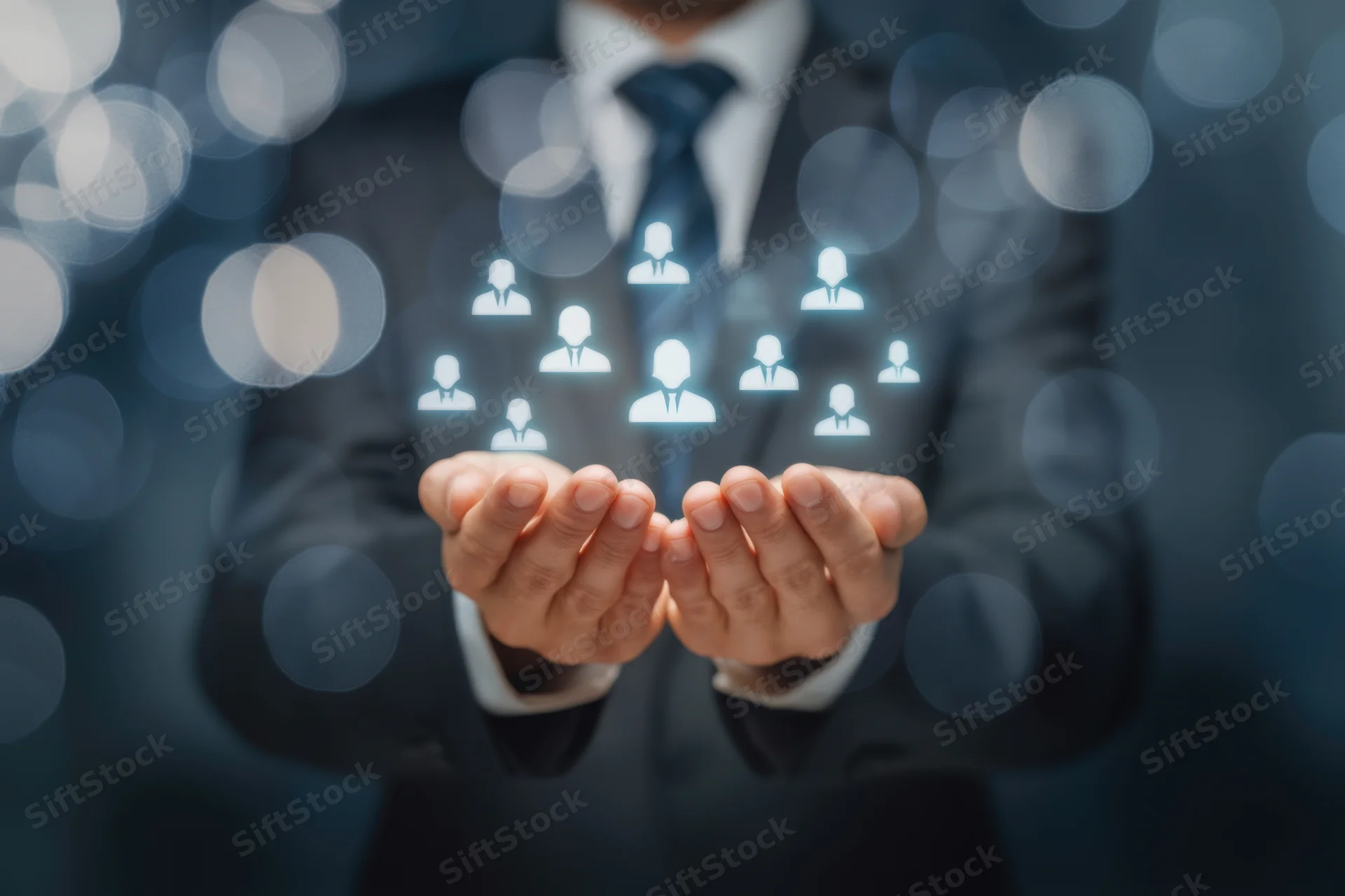 Businessman in suit holding hands out with holographic people icons floating above, against blurred bokeh background