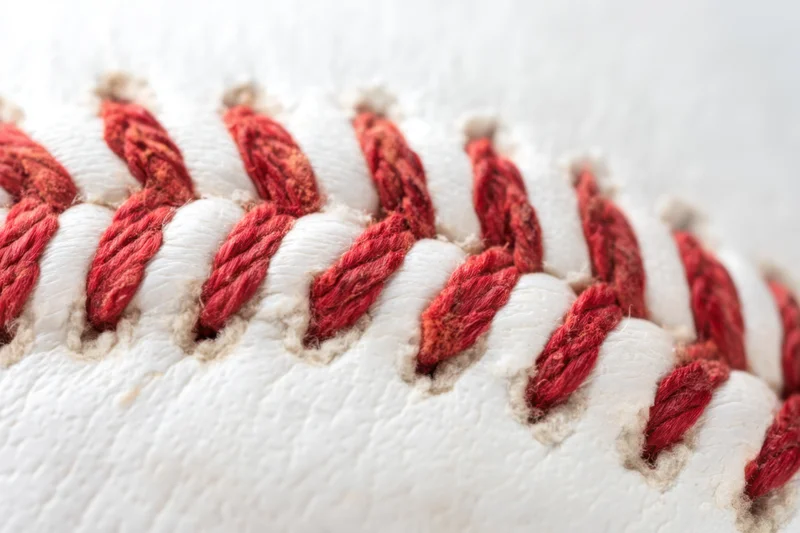 Closeup of a baseball showing detailed red stitching on white leather surface